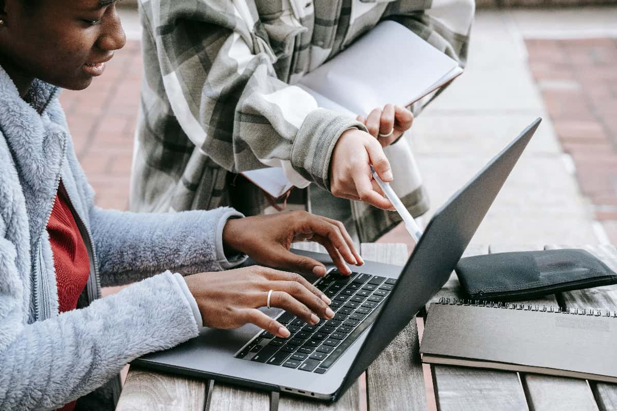One Black American student typing on a laptop screen, while another student points at it with a pen