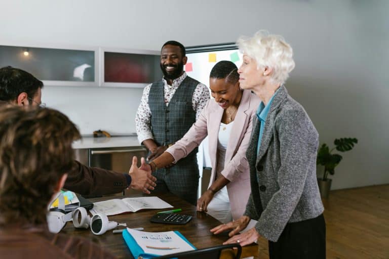 Business professionals of various backgrounds, including older learners, engage in a handshake at a meeting, highlighting teamwork