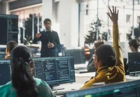A diverse group of students in a coding class, with one raising a hand to engage with the instructor